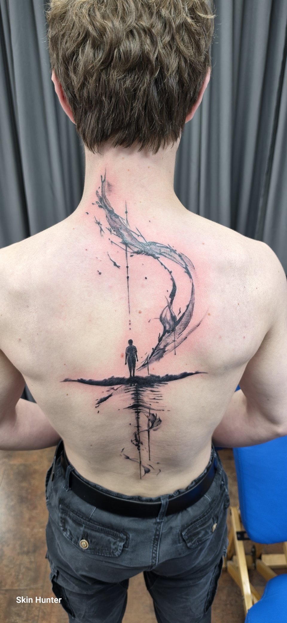 Abstraktes Rücken-Tattoo aus Pinselstrichen mit kleiner Figur über einer Spiegelung entlang der Wirbelsäule