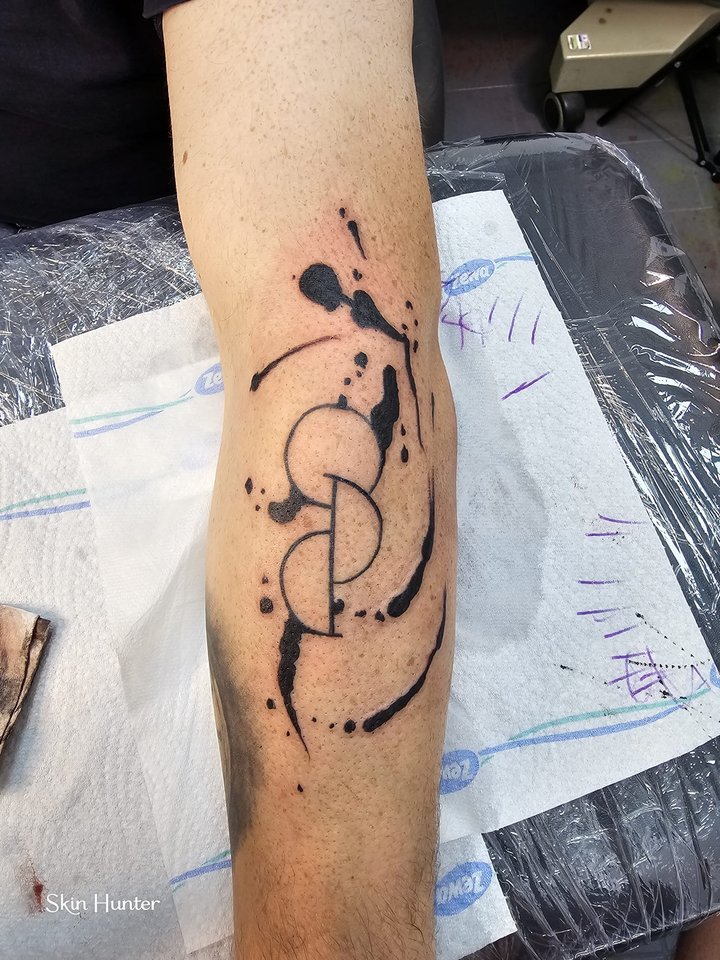 Abstraktes Tattoo mit Kreisen und Tuschespritzern am Unterarm