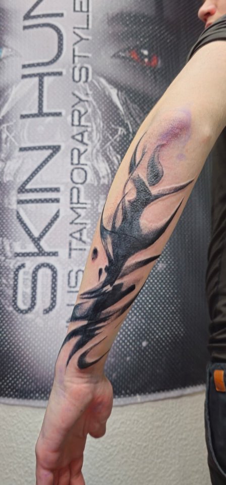 Abstraktes Tattoo aus schwarzen Pinselstrichen am Unterarm vor der Studiowand