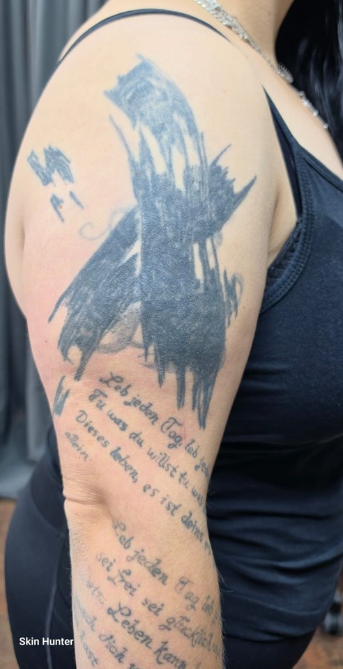 Vorher: Oberarm mit alten, verblassten Tattoos und Schriftzügen vor dem Cover-Up